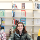 three students sitting at table with bookshelves behind them